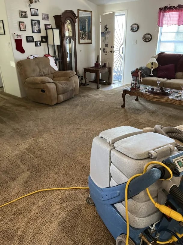 Carpet cleaning machine in use on living room floor with furniture and clocks on walls in background