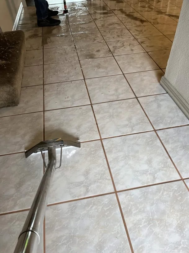 Close-up of grout cleaning tool on ceramic tile floor with brown grout lines