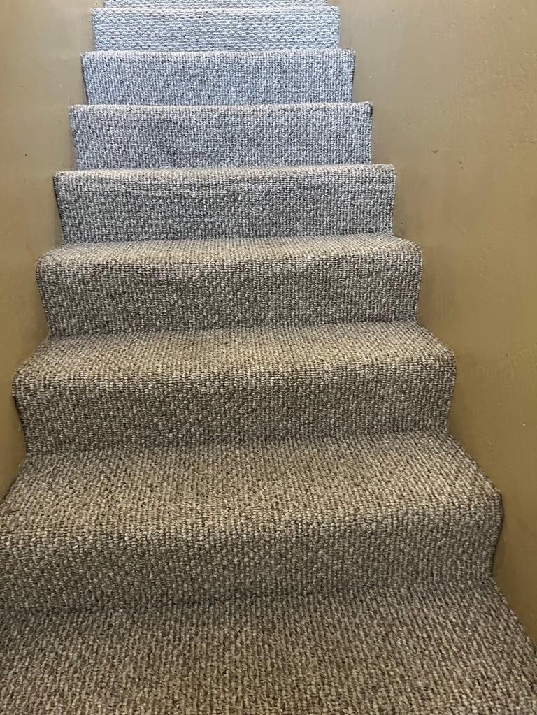 Carpeted staircase with gray textured carpet runner leading upward, beige walls on either side