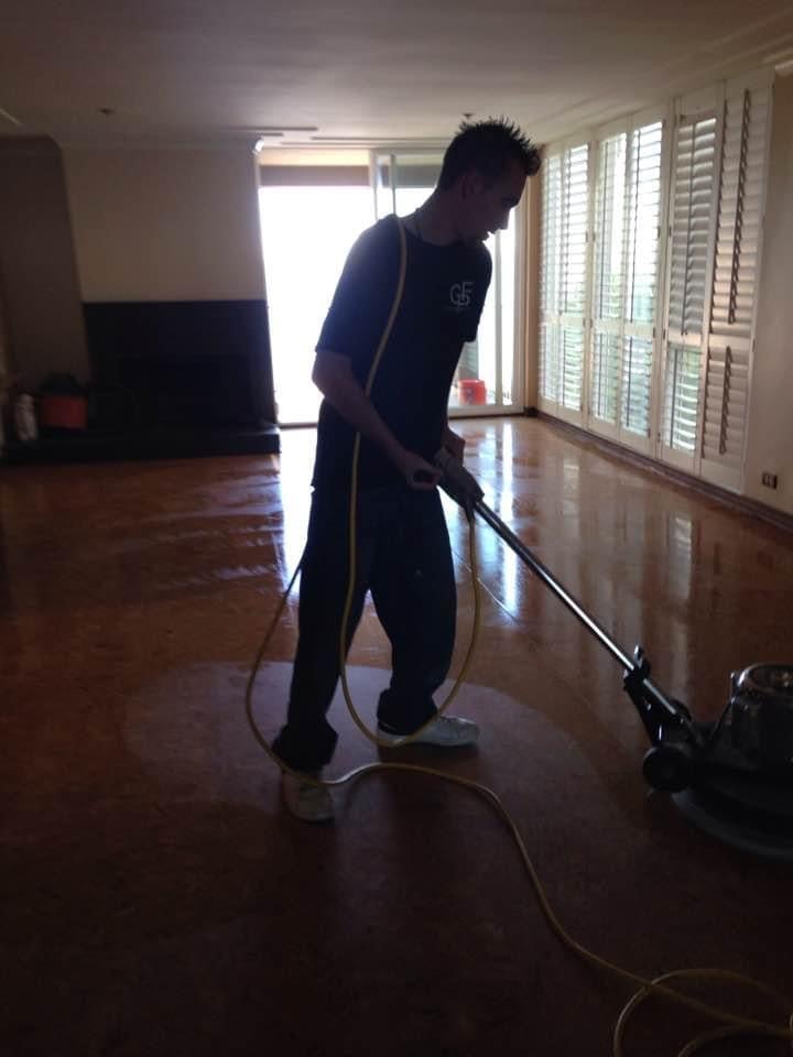 Man in dark blue shirt cleaning wooden hardwood floor with a floor cleaning machine in a bright room