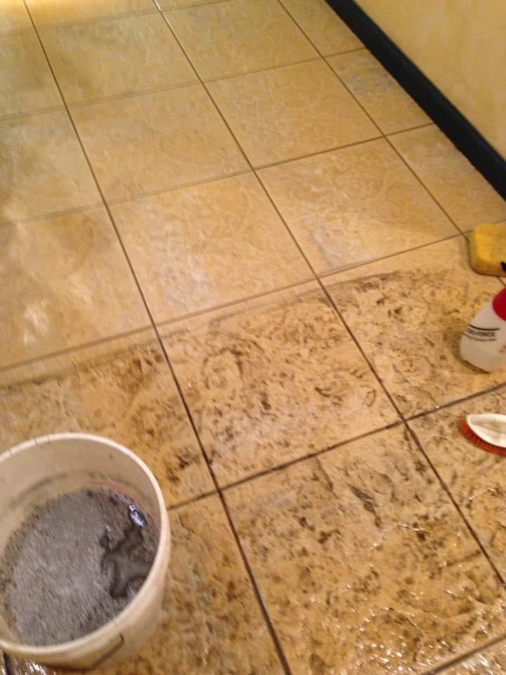 Tiled floor with dirt and cleaning supplies, bucket with dark liquid visible in lower left corner
